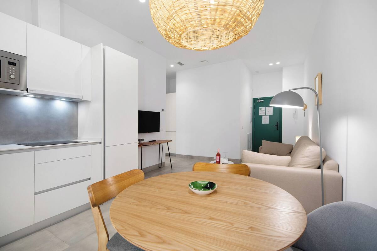 A modern kitchen with white cabinets, a built-in microwave, and a dining area with a round wooden table and chairs.