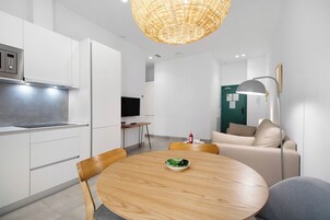 Una cocina moderna con armarios blancos, microondas integrado y un comedor con mesa y sillas de madera redonda.
