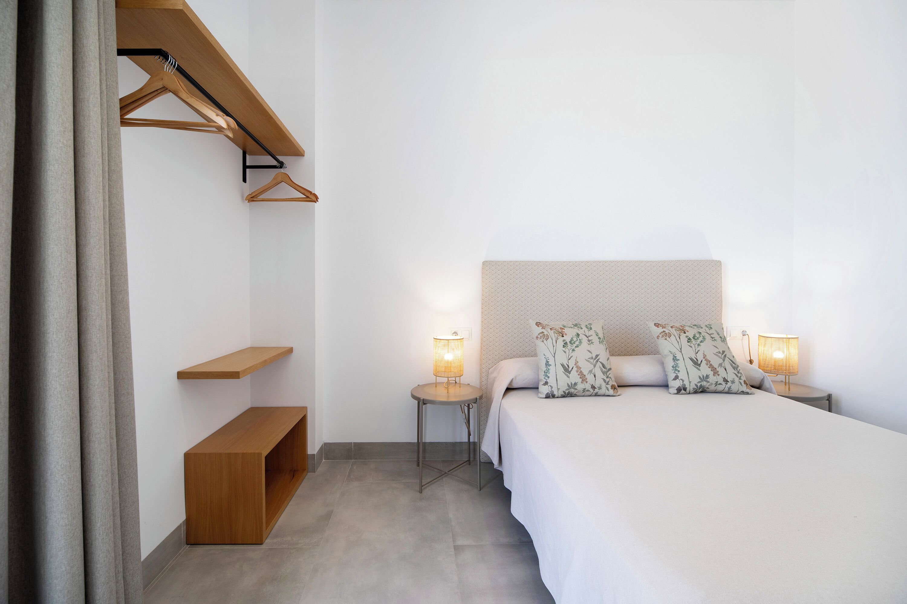 A bedroom with a bed, two bedside lamps, a wooden bench, and a hanging wardrobe.