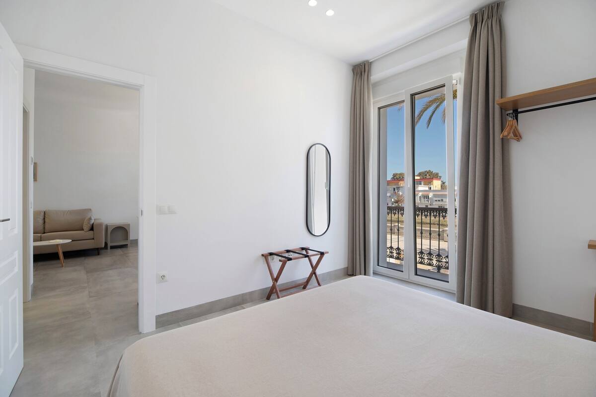 A hotel room with a large bed, a small table, a sofa, and a balcony with a view.
