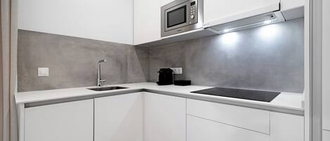 A compact kitchen with white cabinets, a stainless steel microwave, a coffee maker, and a sink.