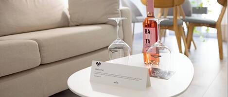 Una sala de estar moderna con un sofá color beige, una mesa redonda blanca con un letrero de bienvenida y una botella de vino.