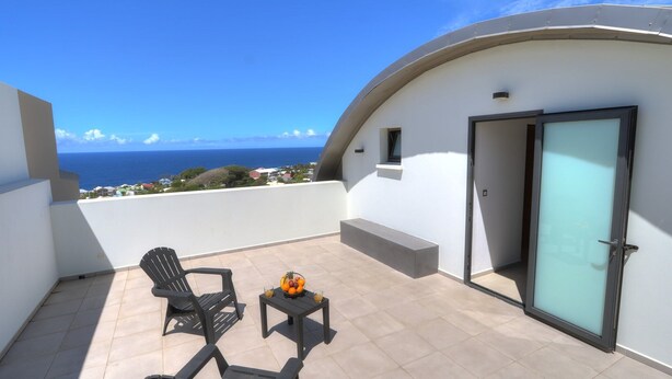 Un balcon avec deux chaises et une petite table, une porte vitrée et une vue sur l’océan.