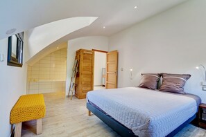 Ein Schlafzimmer mit einem Bett, einer Bank, einem Holzschrank und einer Tür zu einem anderen Raum.