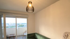 A modern living room with a green sofa, a white bookshelf, and a ceiling light fixture. - Appartement + Parking Privé Gratuit (Marseille)