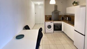 A compact kitchen with a washing machine, a dining table with chairs, and a hanging light fixture. - Appartement + Parking Privé Gratuit (Marseille)