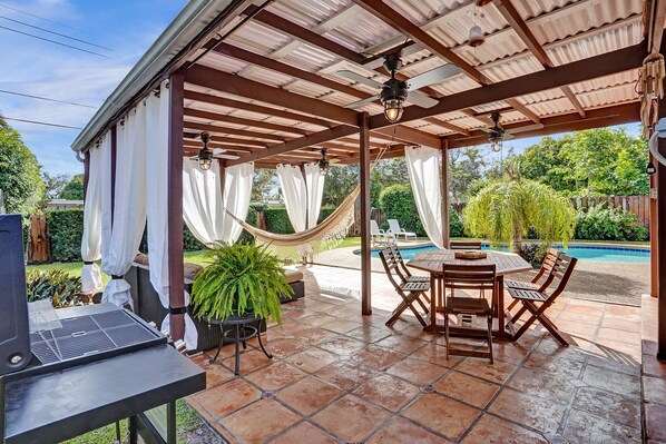 Un patio couvert avec une piscine, du mobilier d’extérieur et un barbecue.