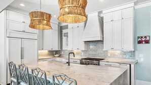 Een moderne keuken met witte kasten, een marmeren eiland en twee rieten hanglampen.