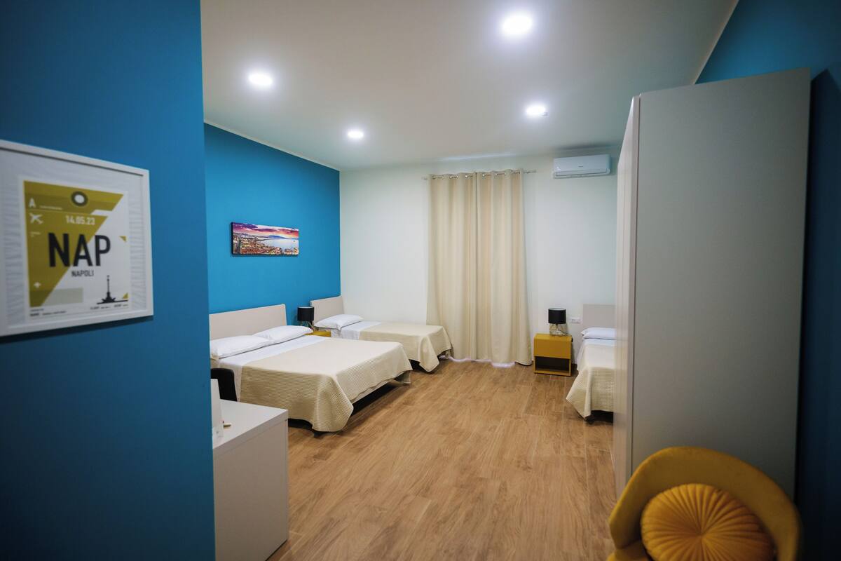 Une chambre d’hôtel avec trois lits, un bureau, une chaise et un tableau au mur.