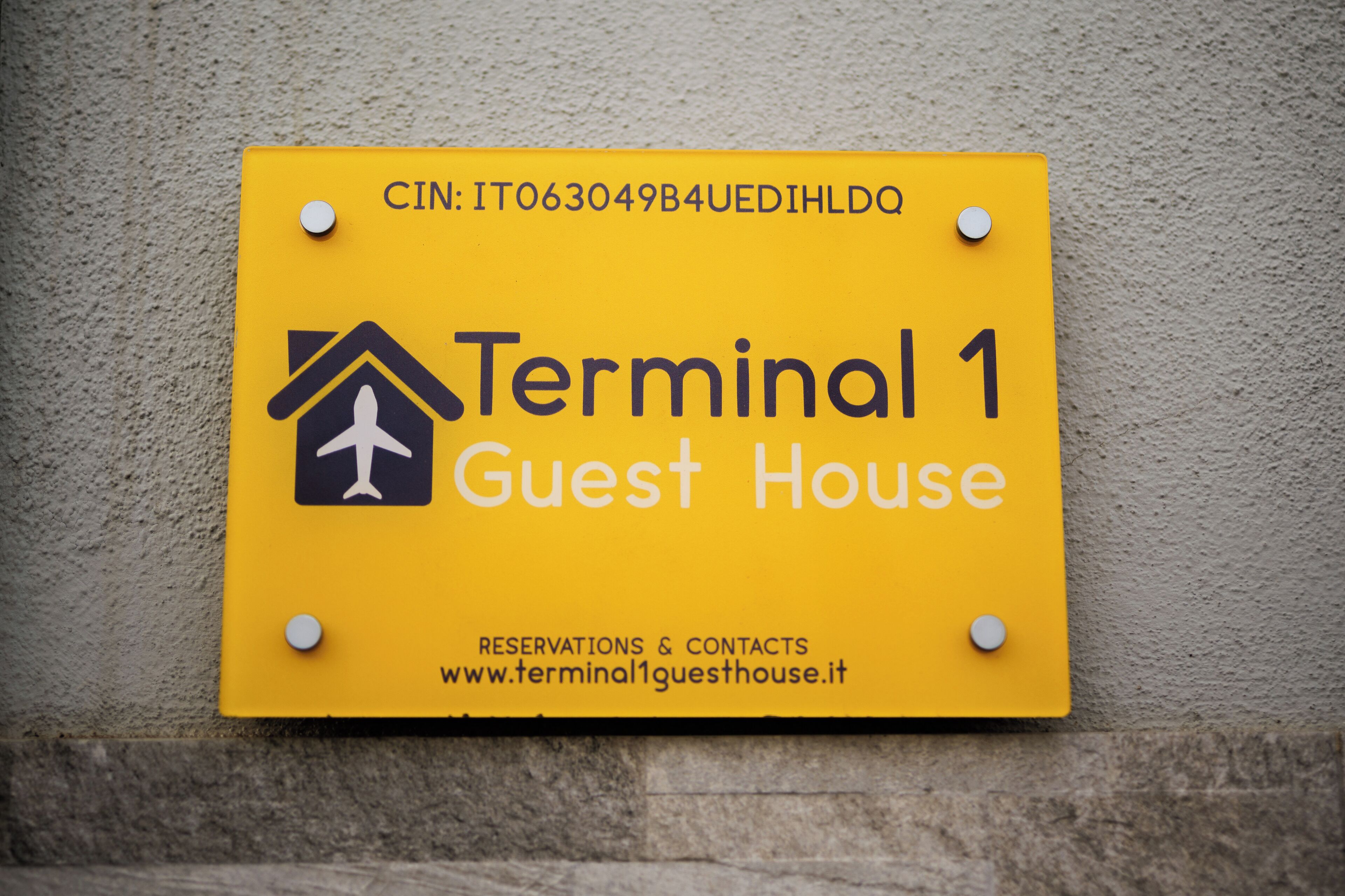 Un panneau jaune indiquant « Résidence pour les voyageurs en transit, terminal 1 » et l’adresse d’un site web.