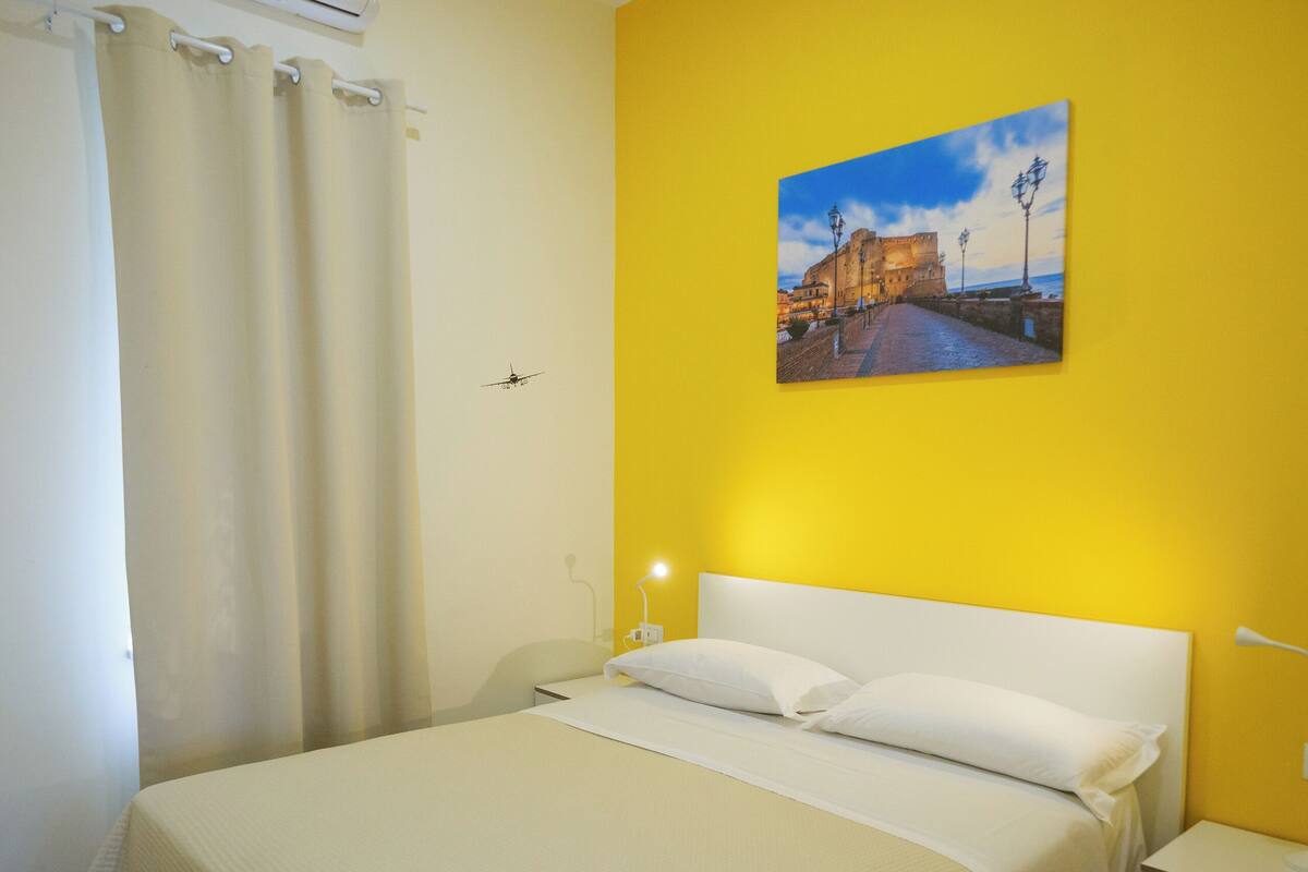 Une chambre d’hôtel avec un grand lit, une table de chevet, une commode, un appareil de climatisation et un tableau au mur.