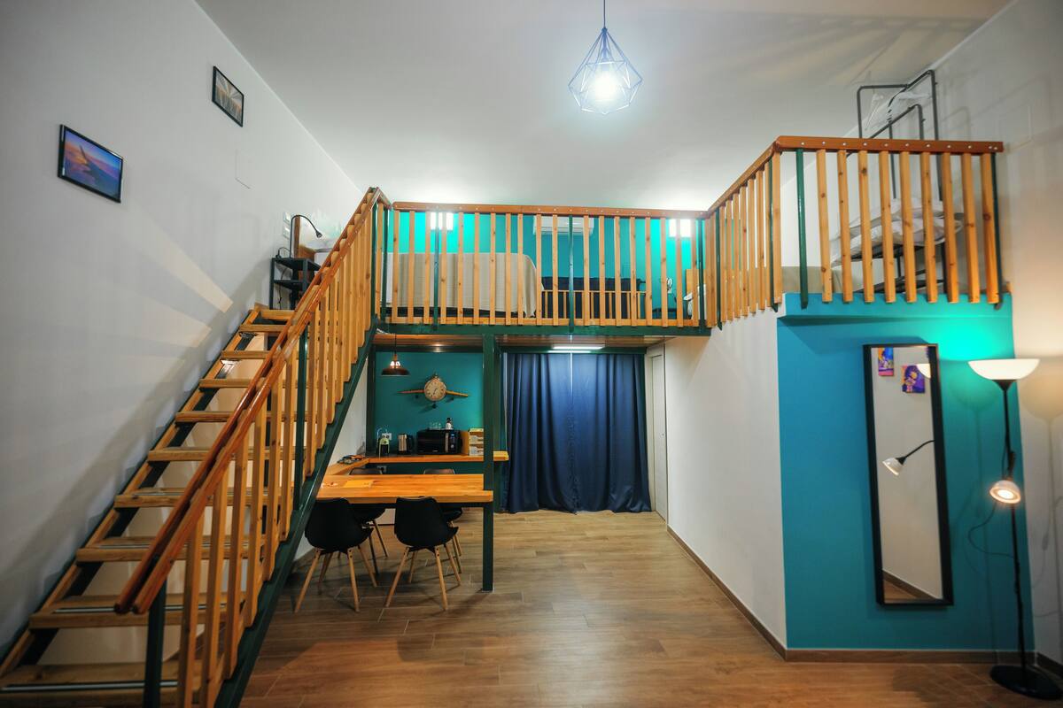 Une pièce de taille modeste, avec un escalier en bois, une petite table à manger et un lit superposé.
