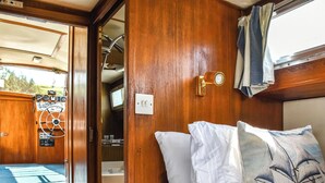 Ein gemütliches Blockhaus-Interieur mit Holzausbau, einem Bett mit weißen und gemusterten Kissen, einem kleinen Badezimmer mit Waschbecken und Spiegel sowie einer Bedienkonsole mit Anzeigen und Lenkrad.
