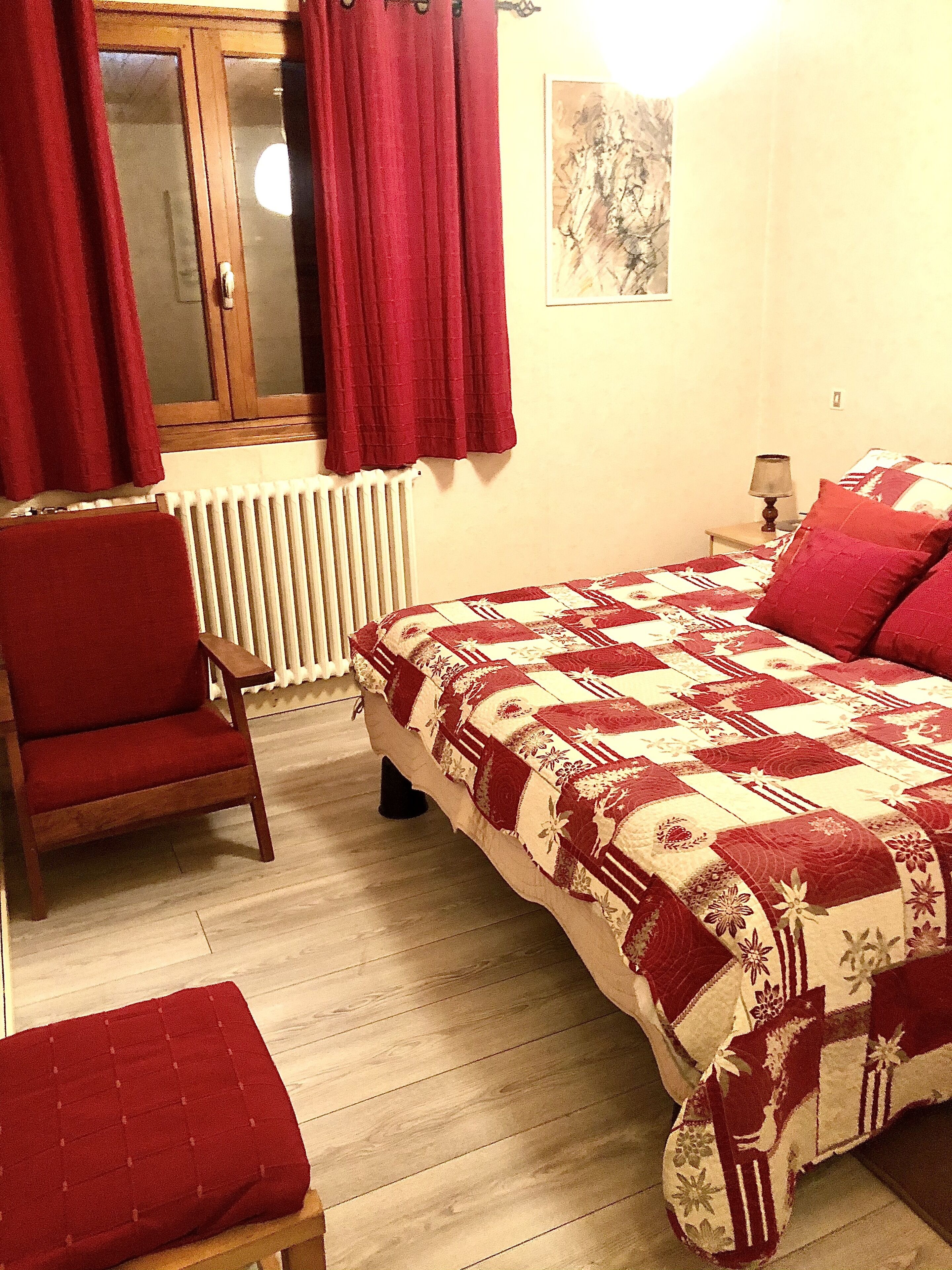 Un dormitorio con cama, una silla, un radiador y una mesita de noche con lámpara.