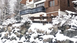 En toetages chalet med træfacade, en balkon og et sneklædt landskab.