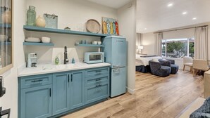A modern kitchen with teal cabinets, a microwave, and a refrigerator. There is a dining area with a table and chairs, and a large window providing a view of the outdoors. - Coastal studio w/ beach access & free parking (San Clemente)
