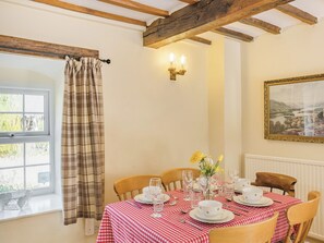 Une salle à manger avec une nappe à carreaux, des chaises en bois et un tableau accroché au mur.