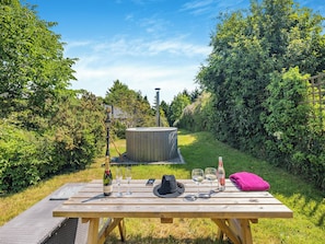 A wooden picnic table with a bottle of champagne, two glasses, a hat, and a pink towel.