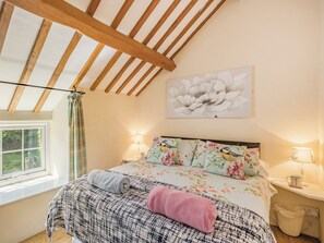 A bedroom with a large bed, floral bedding, a ceiling fan, a window with curtains, and a wall-mounted lamp.