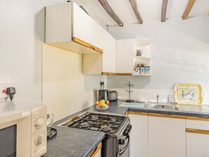 A kitchen with a gas stove, a microwave, and a toaster. There is a fruit bowl on the counter and a shelf with jars and boxes. - Bluebell Cottage - UKC6676 (Betws Yn Rhos)