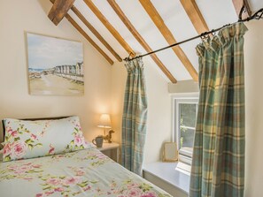 A bedroom with a bed, a nightstand, a lamp, a painting, and curtains. - Bluebell Cottage - UKC6676 (Betws Yn Rhos)