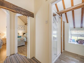 A hallway with a wooden ceiling beam, a glass door leading to a bedroom with a bed and a nightstand, and a window with a view of the outside.