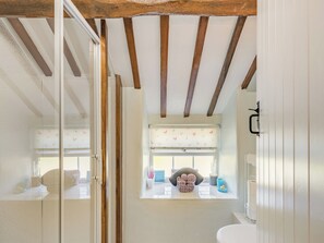 A bathroom with a wooden ceiling, a window with a curtain, and a sink with toiletries.