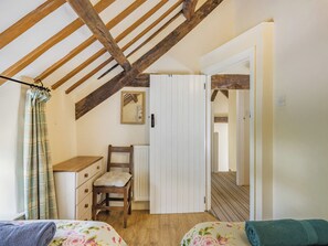 A bedroom with a wooden ceiling, a bed with floral bedding, a chair, a dresser, and a wardrobe.