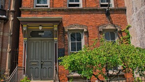 Un immeuble en briques à plusieurs étages, doté d’une porte d’entrée imposante, d’un petit porche et d’une clôture en métal.