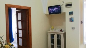 A dining area with a wooden table, chairs, a vase with flowers, a television on the wall, and a cabinet with glass doors.