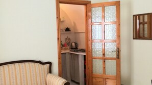 A living room with a sofa, a wooden door leading to a kitchen, and a tiled floor.