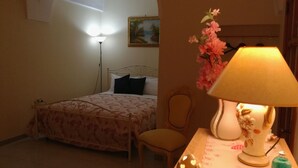 A bedroom with a bed, a chair, a table with a lamp, and a vase of flowers.