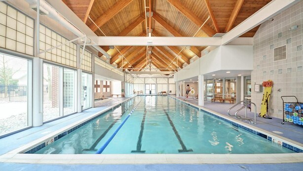 An indoor swimming pool with clear lanes, wooden ceiling beams, and large windows.