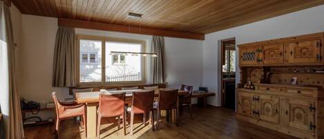 Ein geräumiger Raum mit Holzboden, einem Essbereich mit Tisch und Stühlen, einem Fenster mit Vorhängen und einer Holzkabine mit Schubladen.