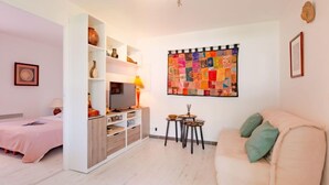 A modern living room with a sofa, a TV, a small table with decorative items, and a colorful quilt on the wall. - Le Mas Kilou by Interhome (Saint Aygulf)