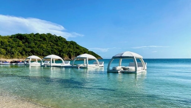 Una playa con agua cristalina y varias estructuras blancas tipo sombrilla.
