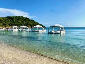 Ein Strand mit klarem Wasser und mehreren weißen Sonnensegeln.