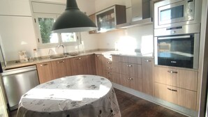 Une cuisine avec des meubles en bois, un four Bosch et une table recouverte d’une nappe à motifs de café.