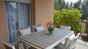 Une terrasse avec une table en bois et des chaises blanches, un pot de fleurs et une vue sur la verdure.