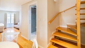 Un interior moderno con una escalera de madera, una silla blanca y una puerta que da a un baño.