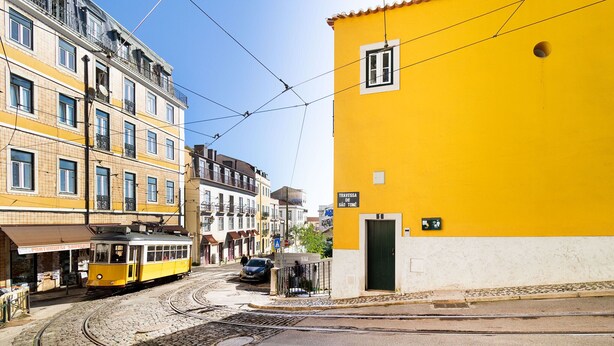 Un edificio amarillo con un letrero que dice "TRAVESSA DE SÃO JOÃO" y un tranvía sobre las vías.