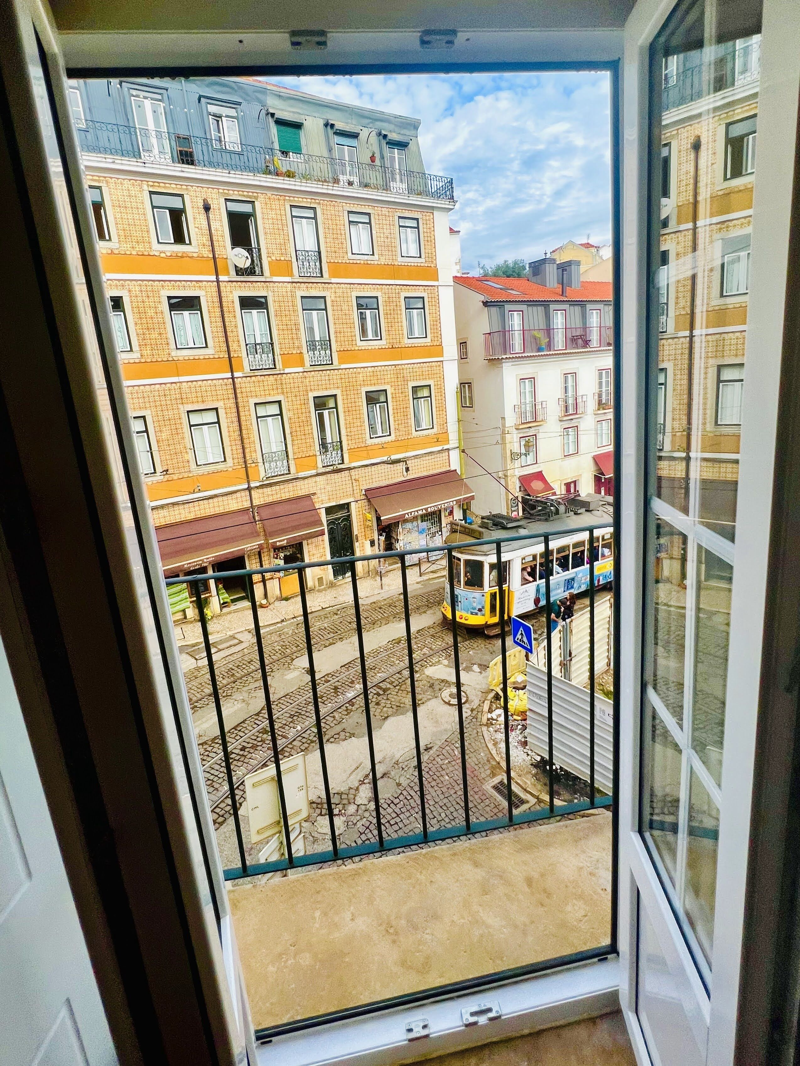 Vista des d'un balcó amb un tramvia passant, edificis amb balcons i un carrer amb botigues.