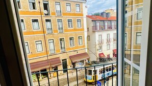 Vista desde un balcón con un tranvía pasando, edificios con balcones y una calle con tiendas.