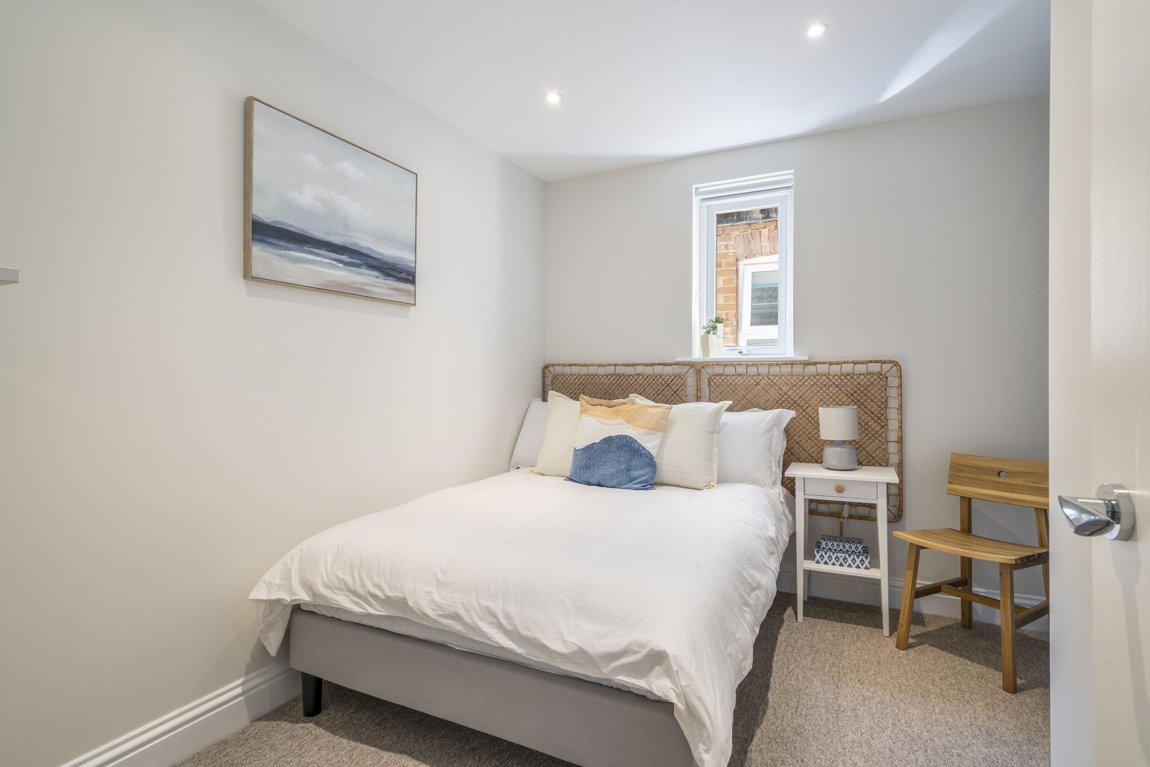 A bedroom with a bed, a bedside table, a chair, a window, and a wall-mounted picture.
