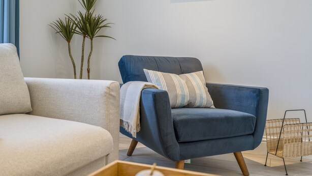 Ein modernes Wohnzimmer mit blauem Sessel, beigefarbener Couch und einem kleinen Holztisch mit Dekoration.