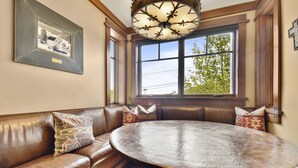 A room with a brown leather sofa, a round wooden table, and a large window with a view of trees. - Arrowleaf by Luxury Mountain Destination (Park City)