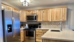 A modern kitchen with wooden cabinets, stainless steel appliances, a central island, and a tiled backsplash. - Cozy, Modern Lakeside Condo (Dillon)