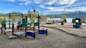 A playground with climbing structures and a wooden bench, set against a backdrop of mountains and a lake. - Cozy, Modern Lakeside Condo (Dillon)