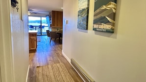 A hallway with wooden flooring, a dining area with chairs and a table, and two wall-mounted posters of Rocky Mountain National Park and Great Sand Dunes National Park. - Cozy, Modern Lakeside Condo (Dillon)