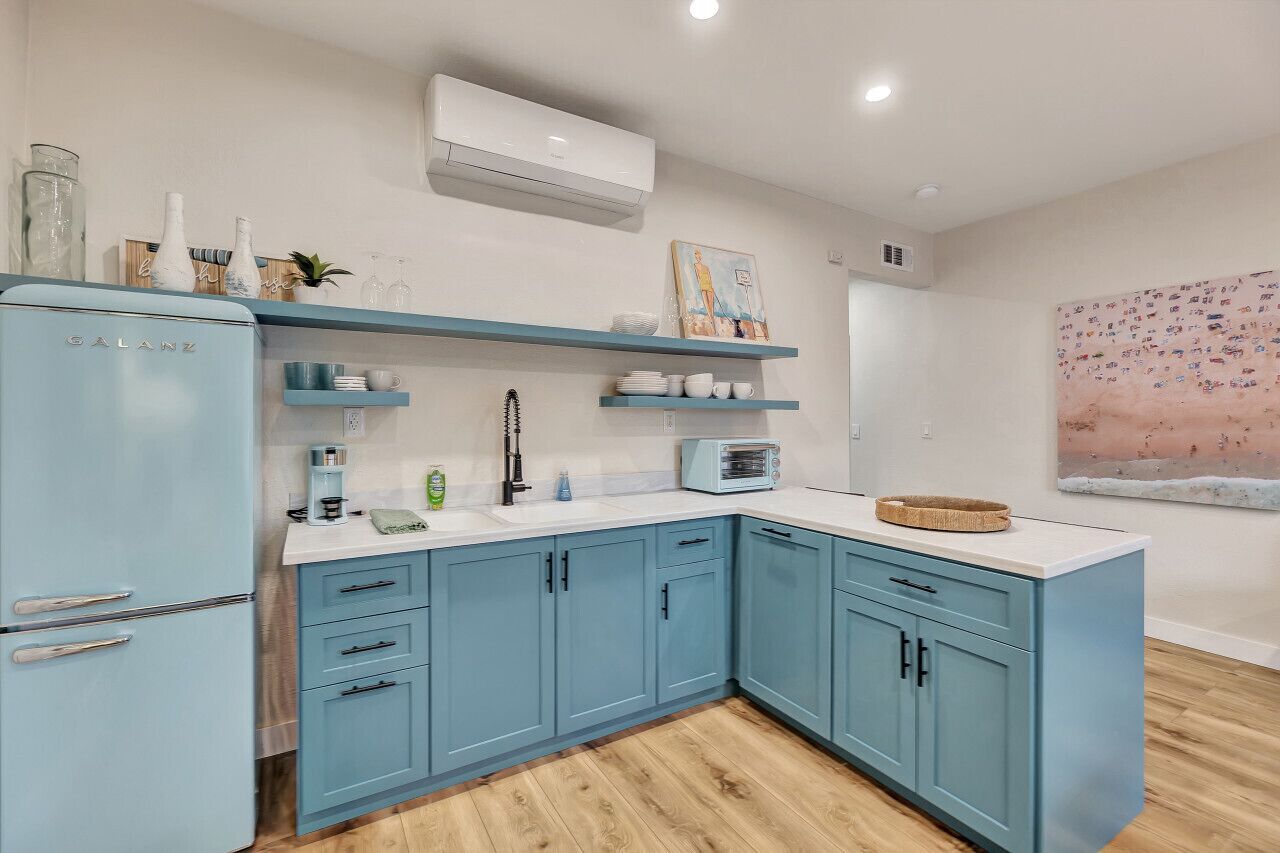 Eine Küche mit hellblauen Schränken, einer weißen Arbeitsplatte und einem weißen Kühlschrank. Ein Toaster, eine Spüle und ein Fenster befinden sich über der Arbeitsplatte.